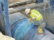 A worker prepares to install a shrink sleeve over the pipe joint to keep dirt and rock away from the connection as the trench is backfilled. Welding then occurs underground within the buried pipe.
