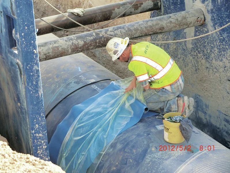 A worker prepares to install a shrink sleeve over the pipe joint to keep dirt and rock away from the connection as the trench is backfilled. Welding then occurs underground within the buried pipe.