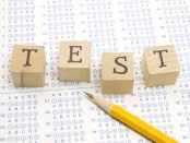 Wooden blocks spell out TEST on a blue bubble or scantron sheet with a number two yellow pencil.