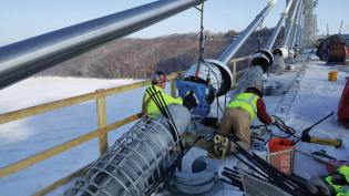 The St. Croix Crossing connects Oak Park Heights, Minnesota, and St. Joseph, Wisconsin. Crews use a hydraulic clamping device (blue) to draw 76 cable strands into a tight circle so dampers can be installed to minimize vibration in the cables due to wind or other loadings.