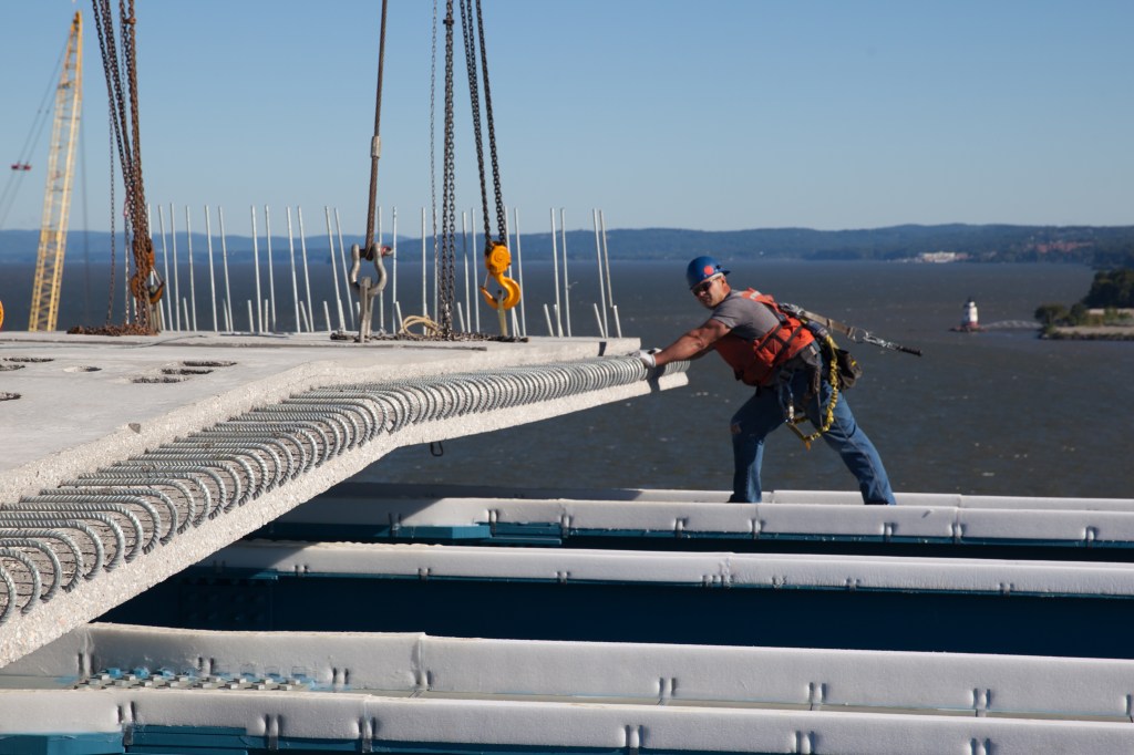 A worker helps guide the placement of a prefabricated concrete road deck panel.
