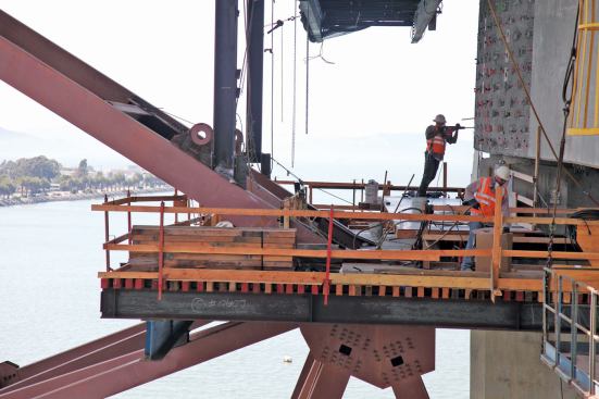 Crews on the pier work platform drill the concrete cap beam in preparation for the bolt fix.