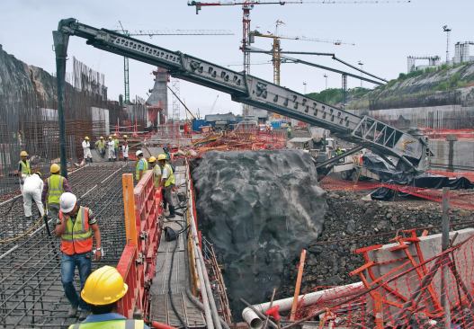A conveyor delivers concrete to the site, which, in places, is a maze of rebar.