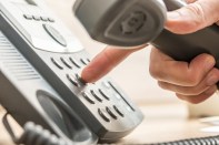 Closeup of male telemarketing salesperson holding a telephone receiver dialing phone number to make a business call.