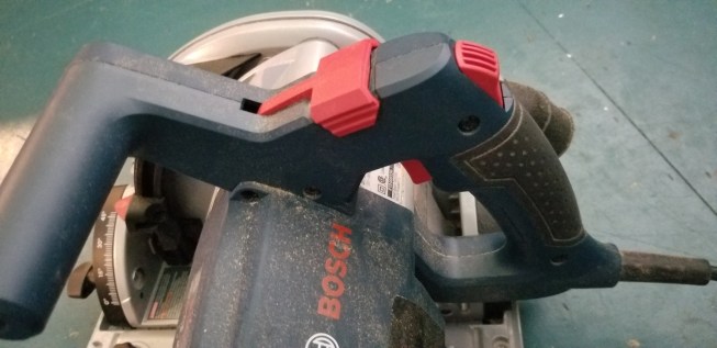 Most of the moving parts are where you want them. The forward red bit locks the saw in the right place to change the blade, the red bit behind that one unlocks the plunge mechanism and the trigger, and the red trigger makes the blade spin.