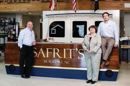 Boat People: The area just offshore from Safrit's Building Supply is a sport fisher's haven, so it made sense to build a showroom sales desk that resembles the stern of a boat. Fred Lund (left) recently came aboard as EVP, while Sue Vaughn (center) just retired after 22 years as credit manager. The boat/desk was the brainchild of Matt Hawkins (right), Beaufort store manager.