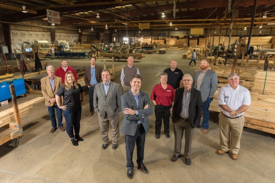 Wilson Lumber President Robb Wilson stands front and center with his executive team. From left, starting with the woman in the second row, they are: Lindsay Wallace (controller), John Marshall (chief operating officer), Debbie Shores (human resources director), and Ken Wilson (co-owner, now retired), and Lee Barton (business development). Third row, starting with the man in the brown jacket: Steve Wilson, (co-owner, now retired), Lee Smith (operations manager), Mark Wilson (commercial millwork sales), Rick Wilson (co-owner, now retired), Jerry Pilman (director of continuous improvement), and Russ Wilson (sales manager).